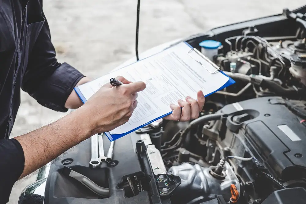 Man with clipboard looking under car hood